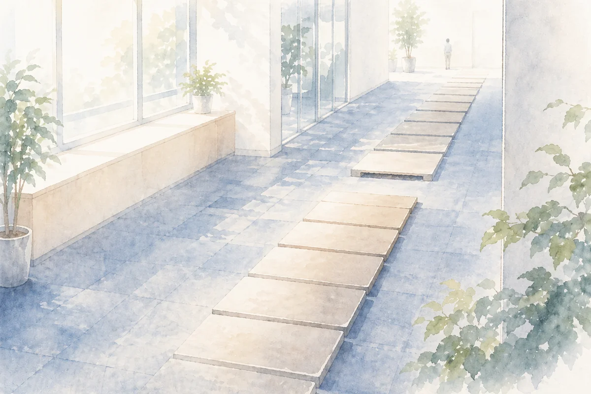 途中で途切れた床の通路が奥へ続く明るい廊下で、契約終了への不安をにじませる構図